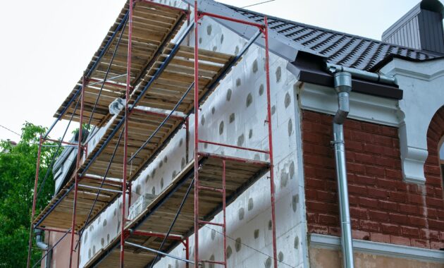 Building facade under renovation works with construction scaffolding frame. Wall insulation with
