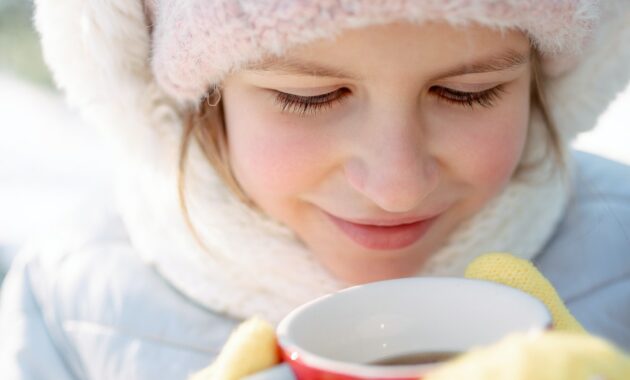 Cute little girl drinks hot tea , frosty weather, steam, red cheeks