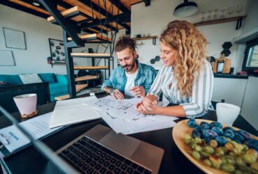 Happy couple using laptop and looking into blueprints of their new home