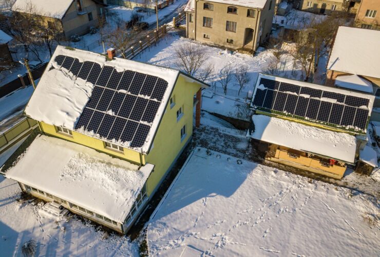 House roof covered with solar panels in winter with snow on top. Energy efficiency and maintenance