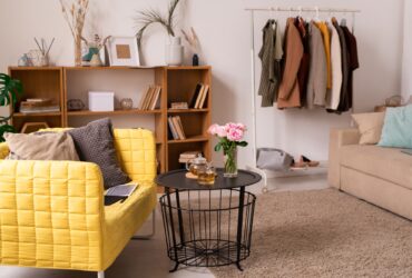 Domestic room interior with couches, shelves, small table and rack with clothes