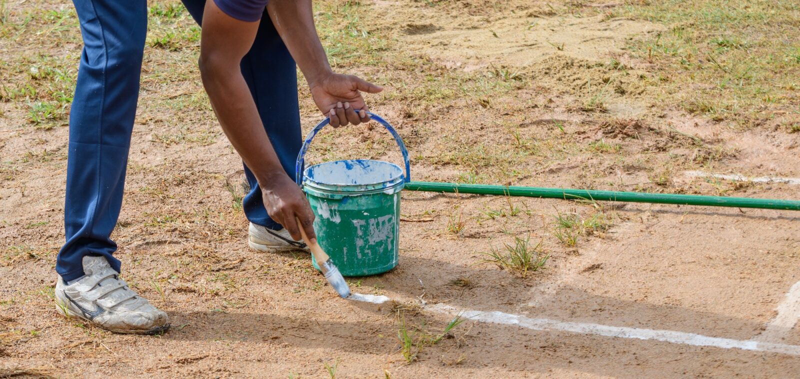 Drawing white lines in a cricket pitch, hands with a brush and white paint, painting straight lines