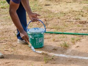 Drawing white lines in a cricket pitch, hands with a brush and white paint, painting straight lines