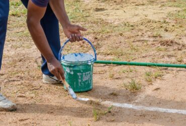 Drawing white lines in a cricket pitch, hands with a brush and white paint, painting straight lines