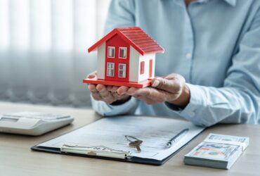 Female real estate agent is use hands holding house of red roof for the concept of real estate