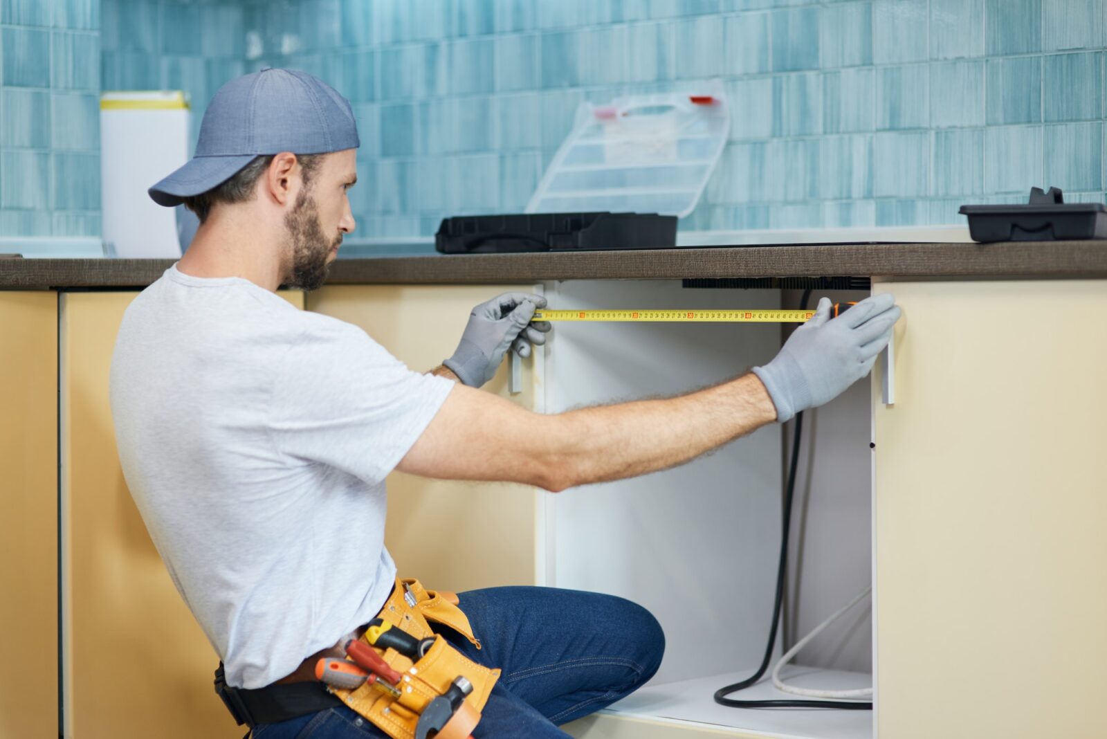 Young repairman, professional plumber using measure tape while doing plumbing work in a new flat