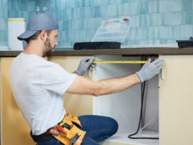 Young repairman, professional plumber using measure tape while doing plumbing work in a new flat