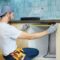 Young repairman, professional plumber using measure tape while doing plumbing work in a new flat