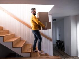 Mature man walking down stairs in house, holding moving boxes.