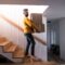 Mature man walking down stairs in house, holding moving boxes.