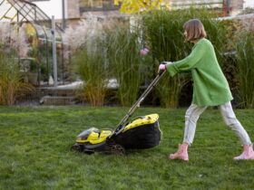 Woman cuts grass with electric lawn mower on backyard
