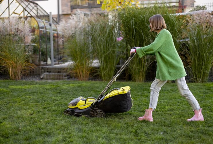Woman cuts grass with electric lawn mower on backyard