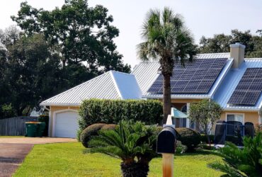 Beach house with solar panels on rooftop for energy surrounded by palm trees for tropical vibes.