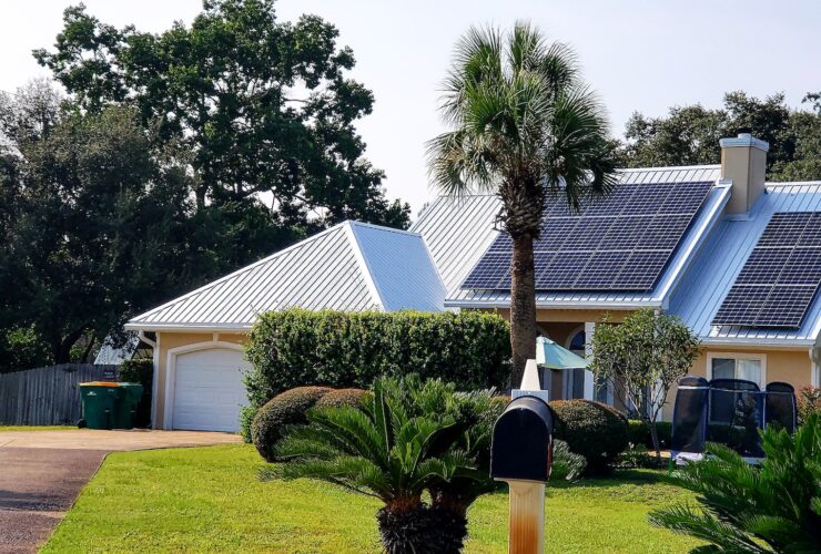 Beach house with solar panels on rooftop for energy surrounded by palm trees for tropical vibes.