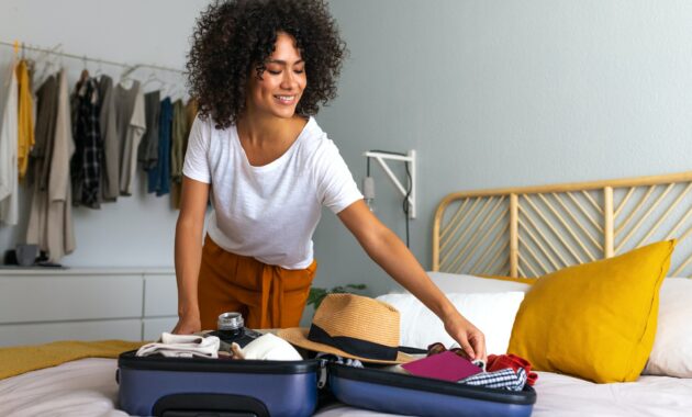 Happy African American young woman packing suitcase at home. Preparing for summer holidays abroad.