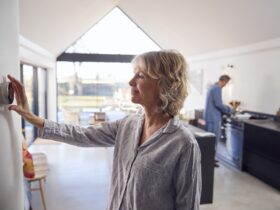 Mature Woman Adjusting Wall Mounted Digital Central Heating Thermostat Control At Home