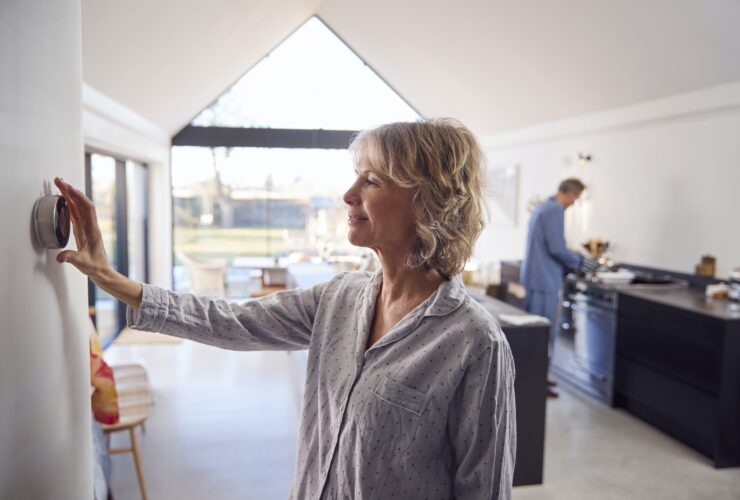 Mature Woman Adjusting Wall Mounted Digital Central Heating Thermostat Control At Home