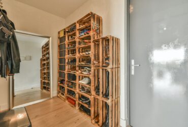 Narrow corridor with shoe rack near doors, white walls and wooden floor