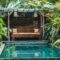Small private swimming pool in Bali house. Green tropical plants around, wooden sofa.