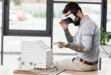 virtual reality architect in virtual reality headset pointing with finger at model of house