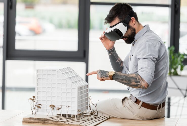 virtual reality architect in virtual reality headset pointing with finger at model of house