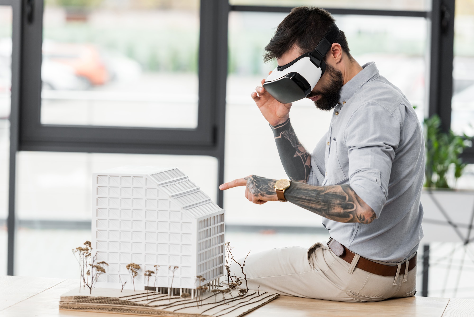 virtual reality architect in virtual reality headset pointing with finger at model of house