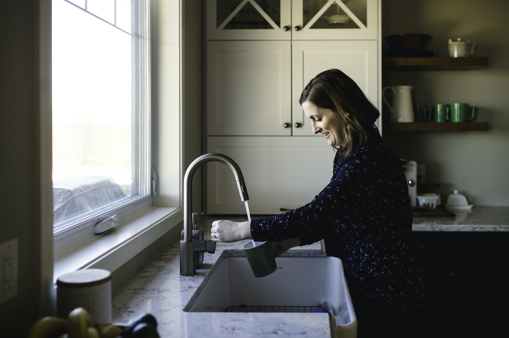 Woman filling up cup at kitchen sink