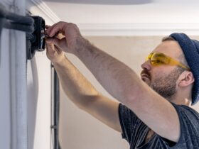 An electrician is mounting electric sockets on the white wall indoors.