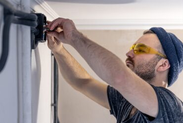 An electrician is mounting electric sockets on the white wall indoors.