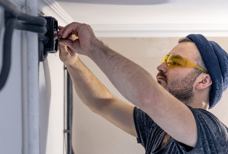 An electrician is mounting electric sockets on the white wall indoors.