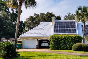Home with beach vibes has solar panels on rooftop surrounded by tropical palm trees.