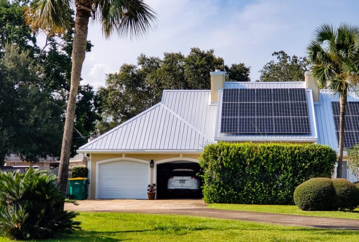Home with beach vibes has solar panels on rooftop surrounded by tropical palm trees.