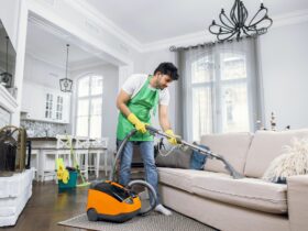 Indian male cleaner cleaning sofa with modern vacuum cleaner