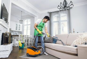 Indian male cleaner cleaning sofa with modern vacuum cleaner