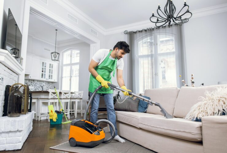 Indian male cleaner cleaning sofa with modern vacuum cleaner