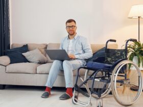 With laptop on the legs. Disabled man in wheelchair is at home