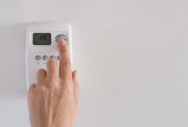 Woman’s hand adjusting digital thermostat settings