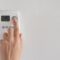 Woman’s hand adjusting digital thermostat settings