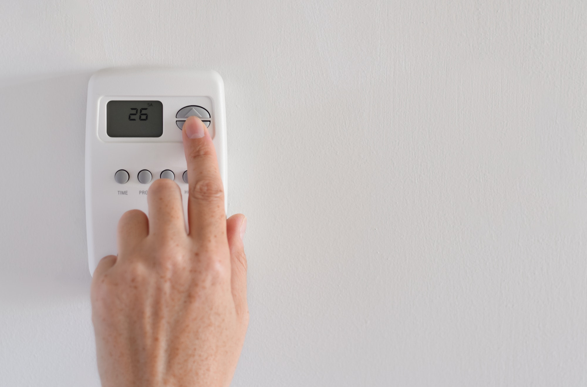 Woman’s hand adjusting digital thermostat settings