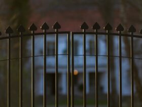 Beautiful and classy ornamented steel fence gate to an impressive old big white house with garden