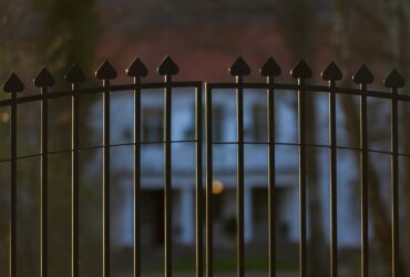 Beautiful and classy ornamented steel fence gate to an impressive old big white house with garden