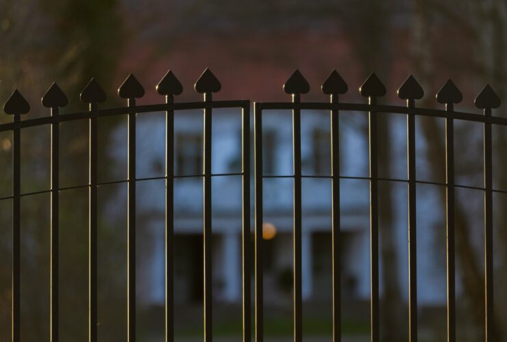 Beautiful and classy ornamented steel fence gate to an impressive old big white house with garden