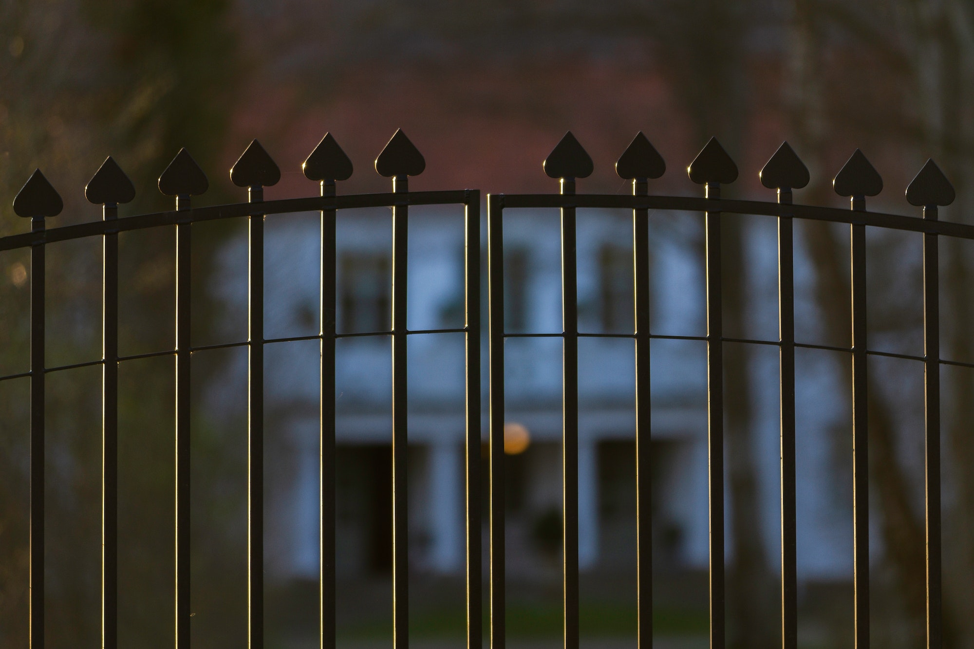 Beautiful and classy ornamented steel fence gate to an impressive old big white house with garden