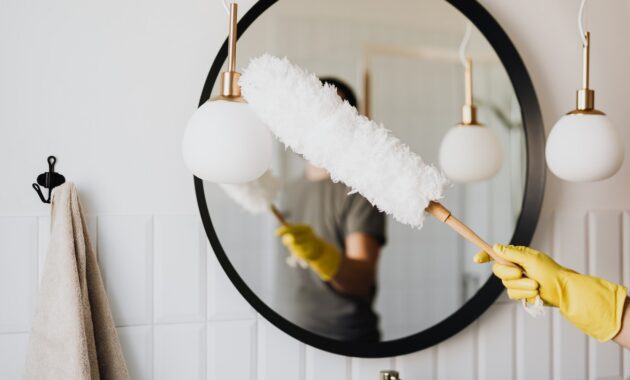 A Person Dusting A Mirror In The Bathroom