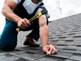 cropped view of handyman in uniform holding hammer while repairing roof