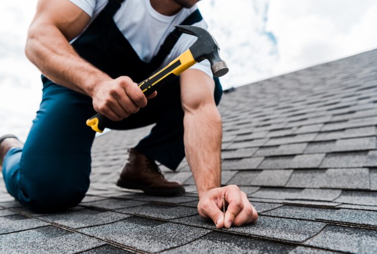 cropped view of handyman in uniform holding hammer while repairing roof