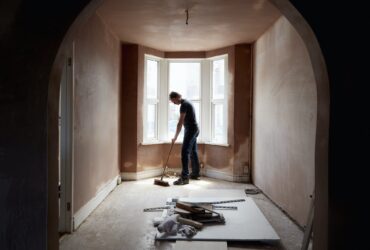 A builder sweeping and tidying up in a renovated replastered house with an archway.