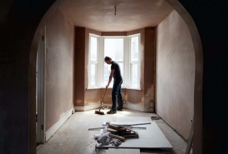 A builder sweeping and tidying up in a renovated replastered house with an archway.