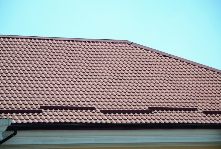 A fragment of a roof from a metal tile of dark red color. Quality Roofing