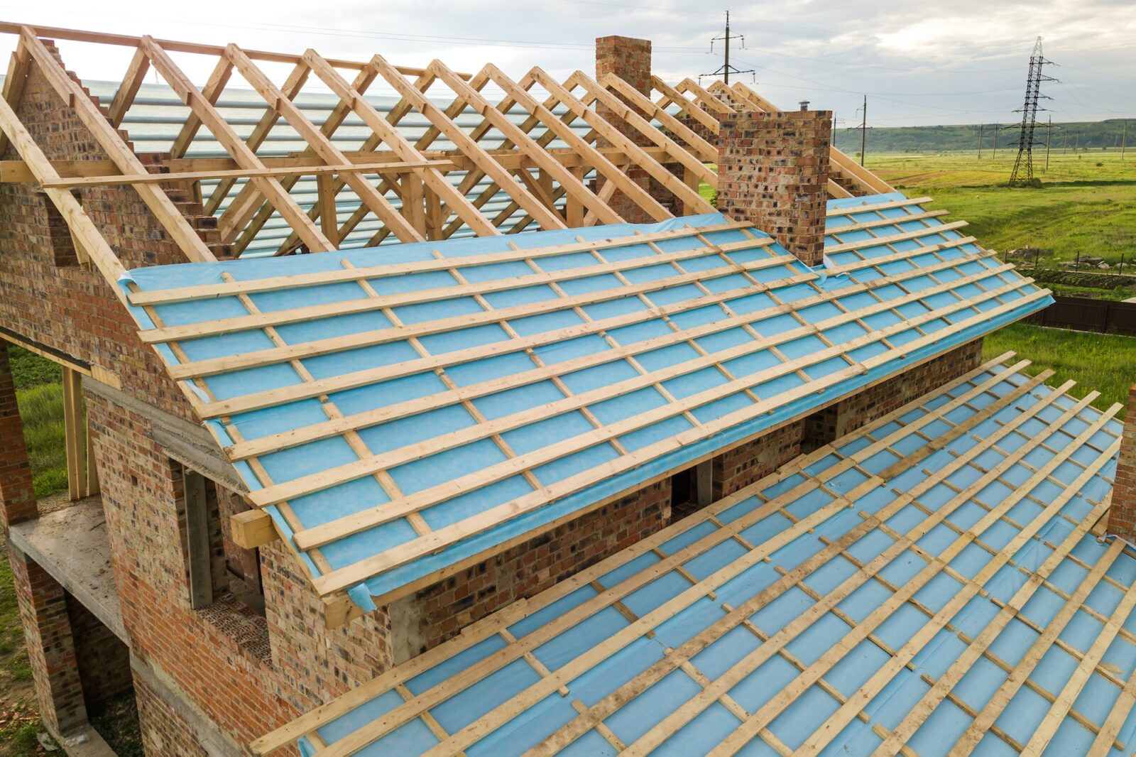 Aerial view of a brick house with wooden roof frame under construction.